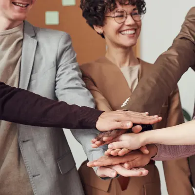 Hands stacked on top of each other with person smiling behind